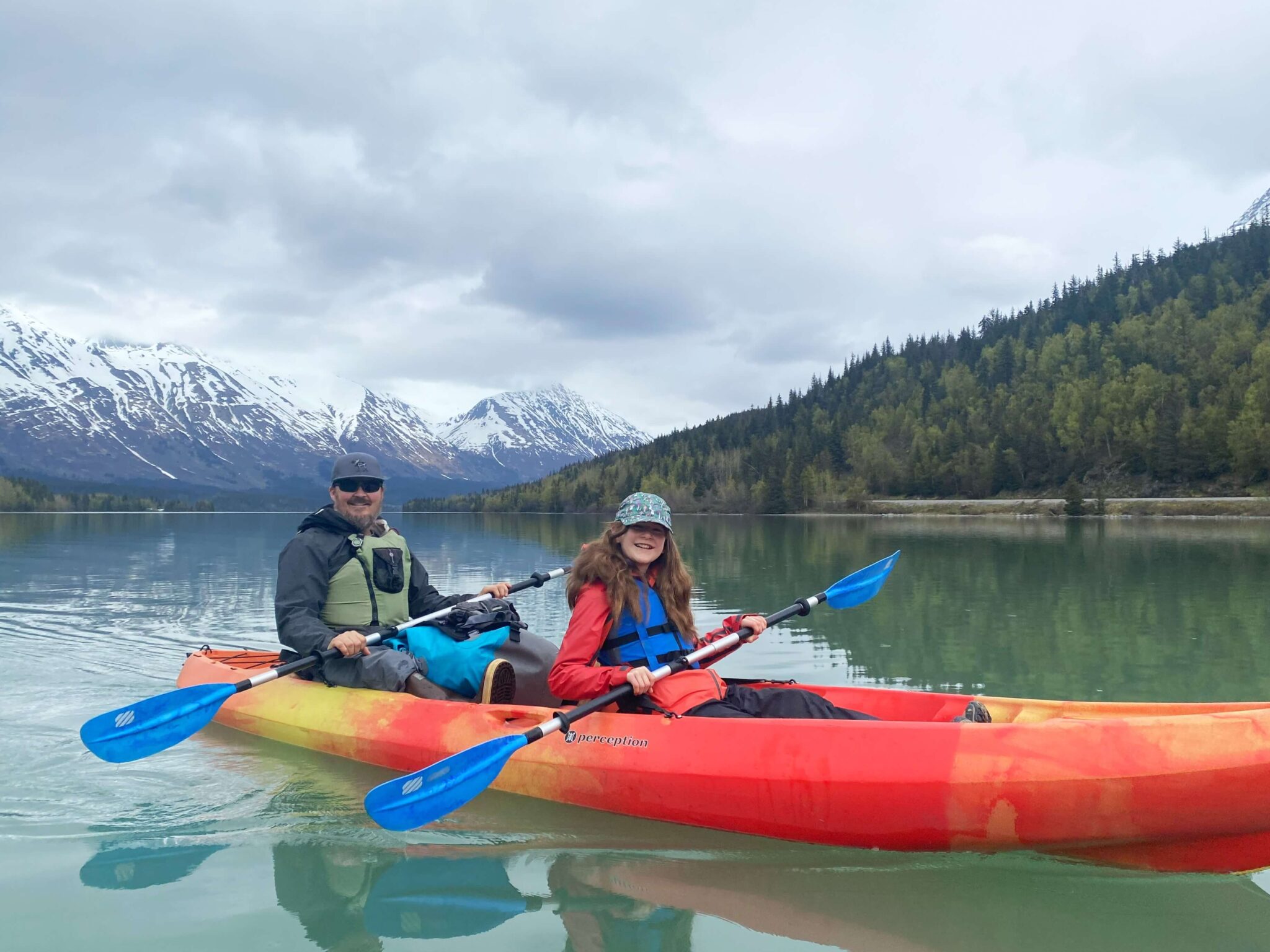 Father and daughter kayaking on glassy water on an Alaskan lake.