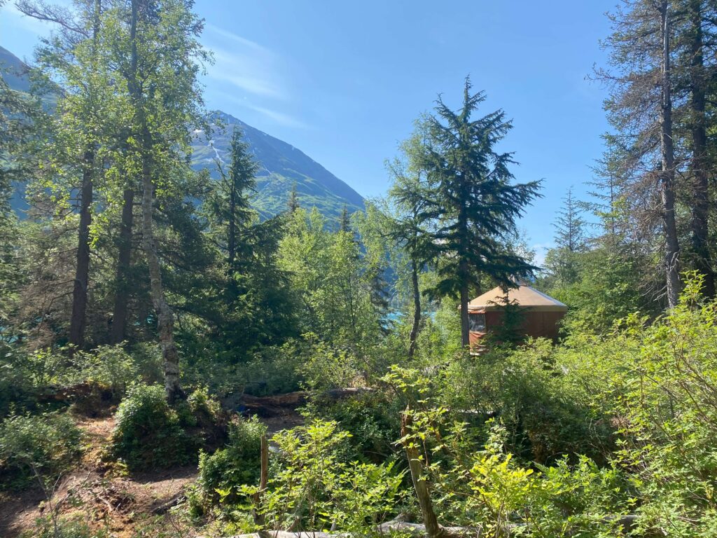 Cozy yurt nestled in the Alaskan wilderness with mountains and turquoise lake in the background